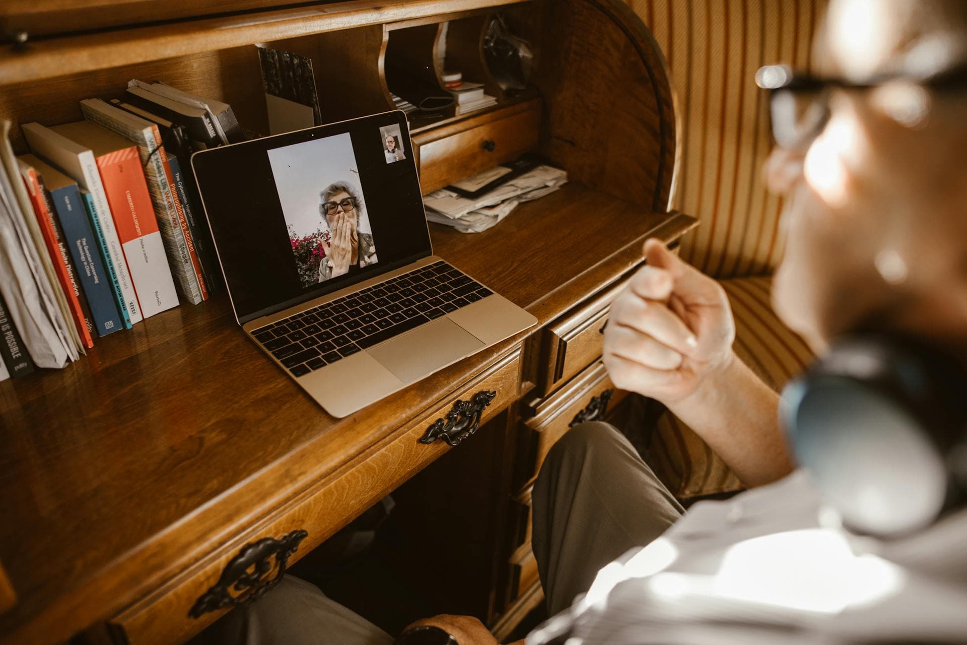 Hands at a laptop showing a video call on screen in a bright workspace - remote-first collaboration